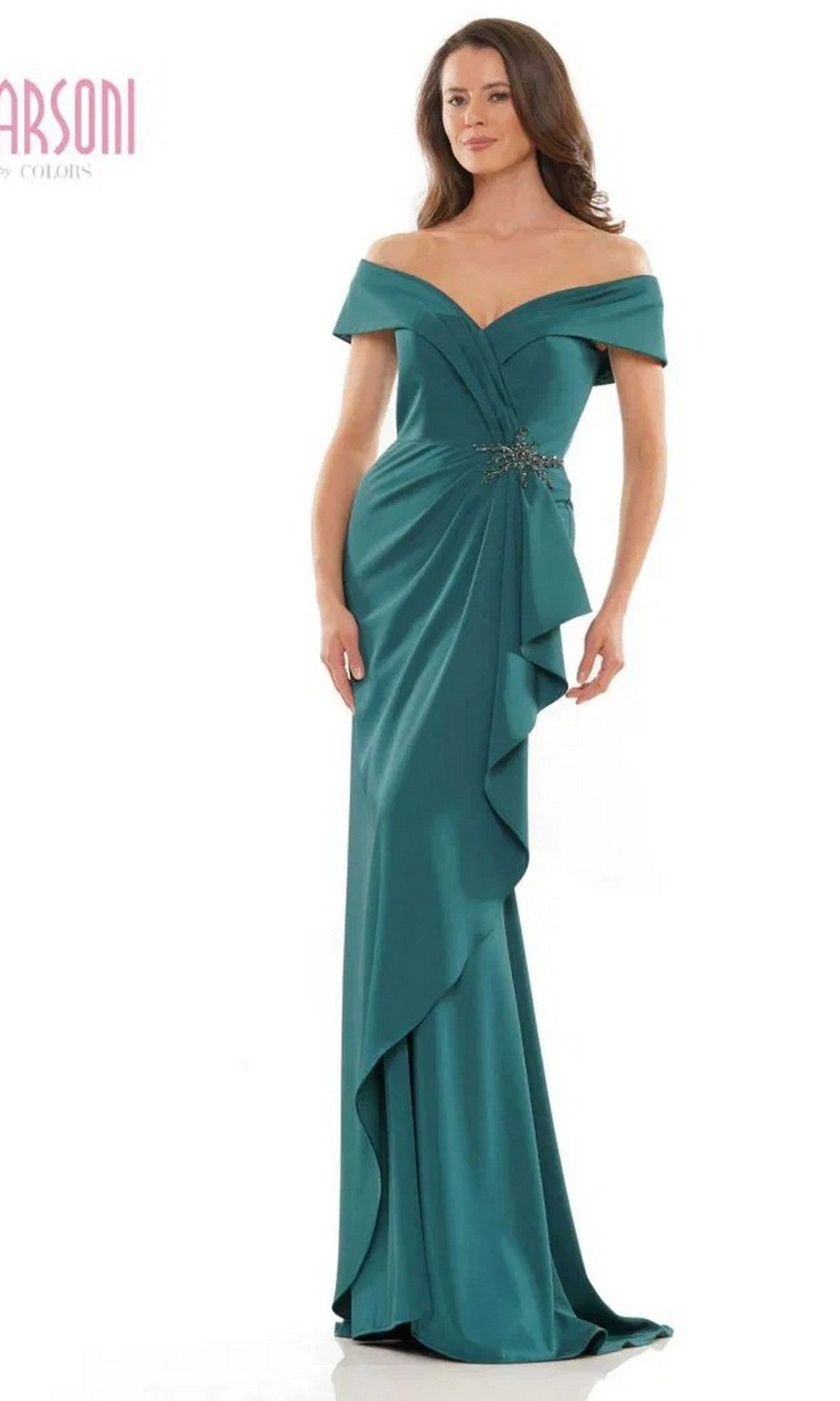 A woman wearing the Marsoni MV1180 Long Formal Dress in forest, featuring an off-the-shoulder neckline, decorative brooch, beaded waistline, and ruffled drape detail, stands against a plain white background.